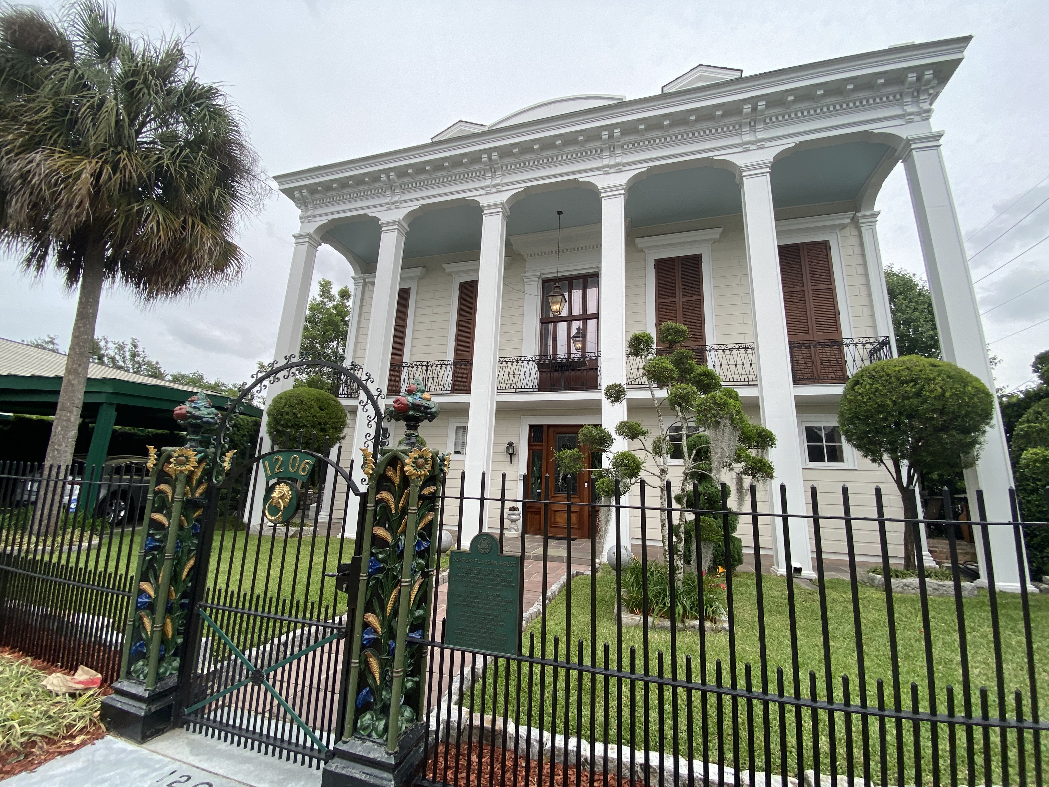 The historic Greek Revival Dufour-Plassan House with tall white columns and an ornate iron gate in Bayou St. John, New Orleans