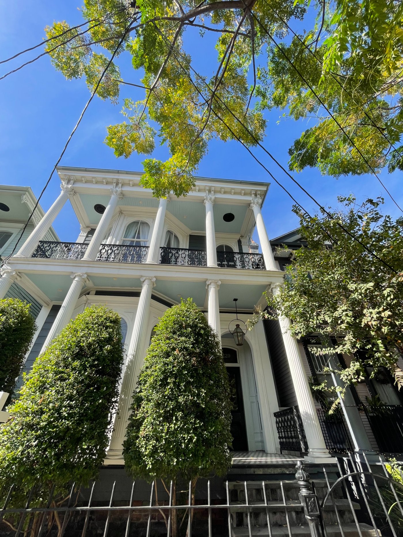 A double-gallery Greek Revival home with white Ionic and Corinthian columns, iron galleries, and topiary in the Lower Garden District, New Orleans